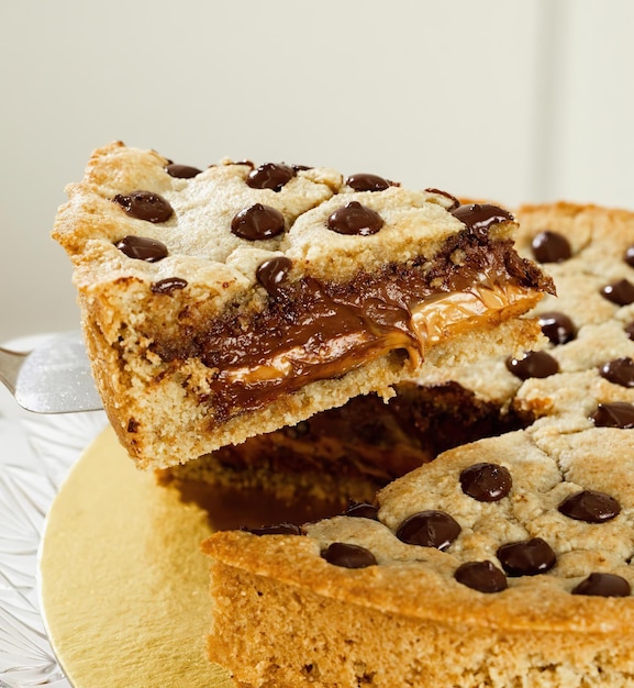 A piece of chocolate chip cookie cake is being cut into slices.