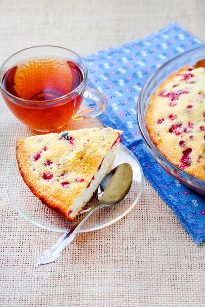 Piece of cowberry pie on glass plate and cup of tea