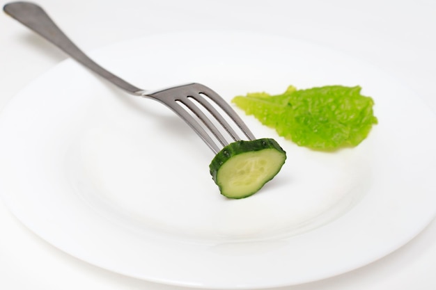 A piece of cucumber and a leaf of lettuce in a white plate on a wine The concept of diet healthy eating weight loss vegetarianism refusal to eat