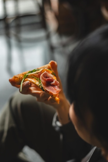 Photo a piece of delicious pizza in hands on a dark background