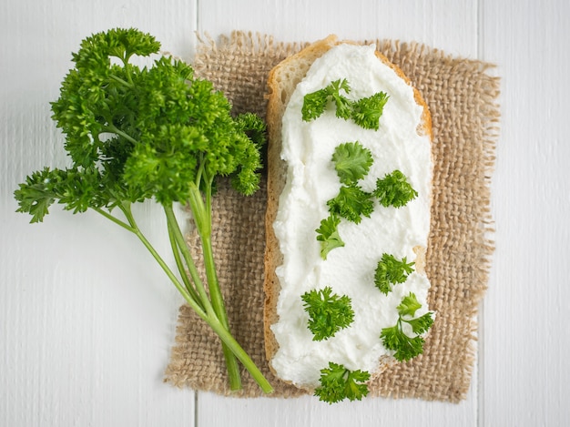 A piece of fresh bread with curd cream and a branch of parsley on a rustic table.