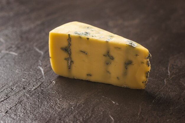 A piece of fresh cheese with blue mold on a stone table. Cheese delicacy. A useful mold