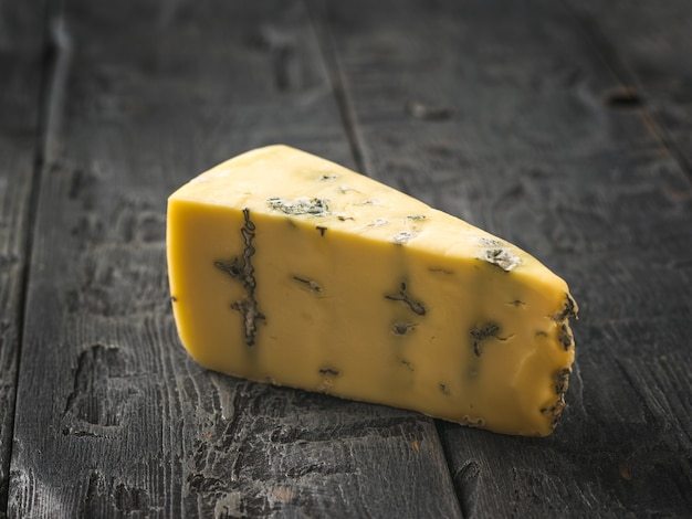 A piece of fresh cheese with blue mold on a wooden table. Cheese delicacy. A useful mold