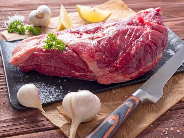 향신료, 허브 및 야채로 둘러싸인 양피지에 신선한 생고기 한 조각이 놓여 있습니다. 칼이 근처에 있습니다. 측면보기. 식품 구성