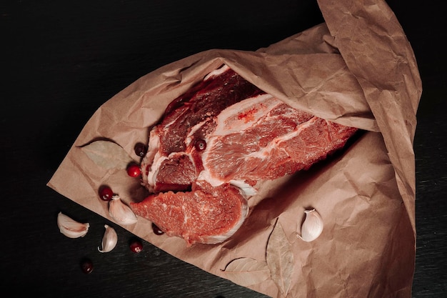 A piece of fresh Raw meat wrapped in kraft paper, garlic cloves, Bay leaf, spices are on the table, close up