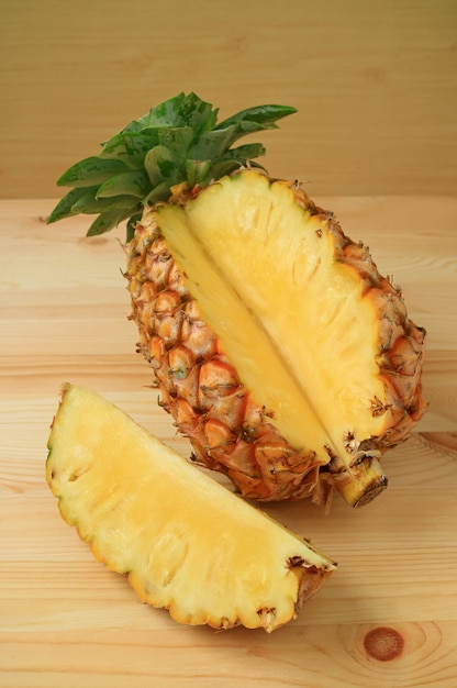 Piece of fresh ripe pineapple cut from the whole fruit isolated on wooden table