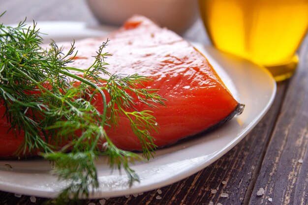 A piece of fresh salted salmon with a sprig of dill olive oil in the background