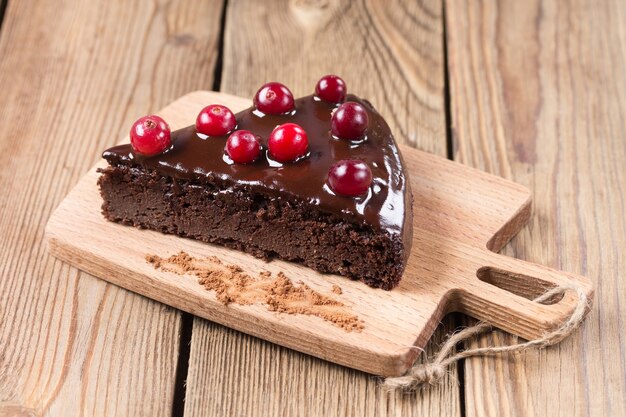 Photo a piece of gluten-free cake in chocolate, decorated with cranberries, on the kitchen board, on a wooden background. healthy desserts.