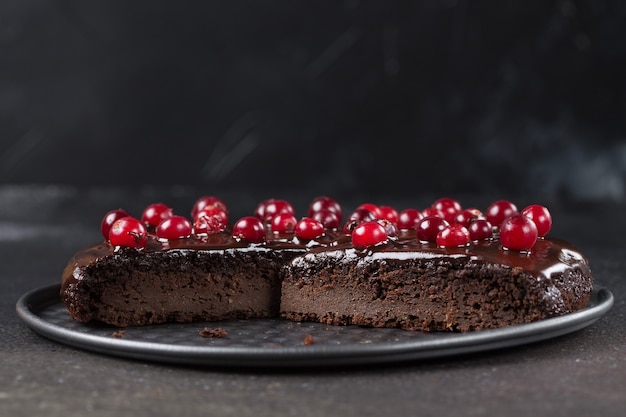 A piece of gluten-free cake in chocolate, decorated with cranberries, on a tray, on a black background. Copy space. Healthy eating.