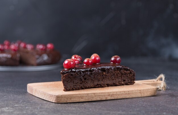 Photo a piece of gluten-free chocolate cake decorated with cranberries on the kitchen board, on a black background. healthy eating. copy space