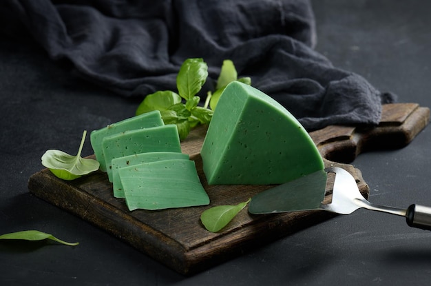 A piece of green cheese with basil on a brown wooden board black background