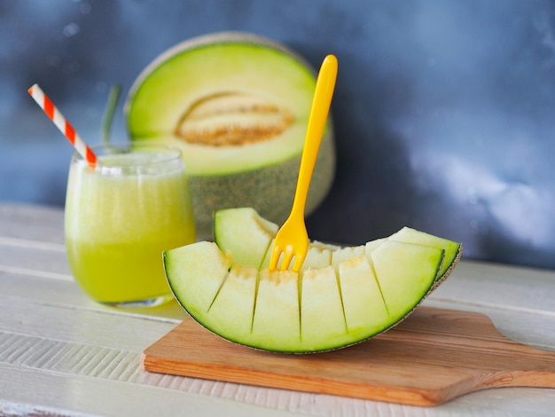 Piece of green melon fruit or honeydew on wooden chopping board and a glass of melon juice