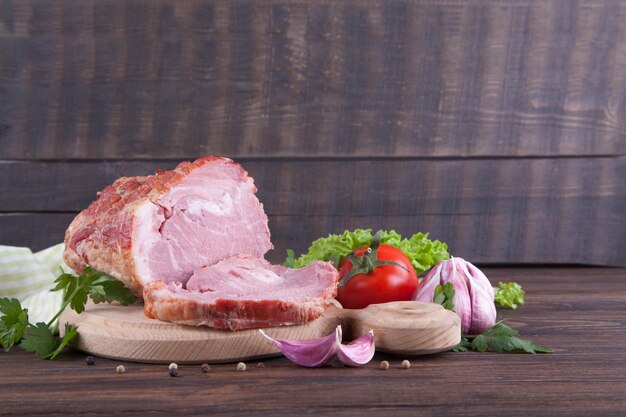 A piece of ham and vegetables on a wooden background. Meatworks product