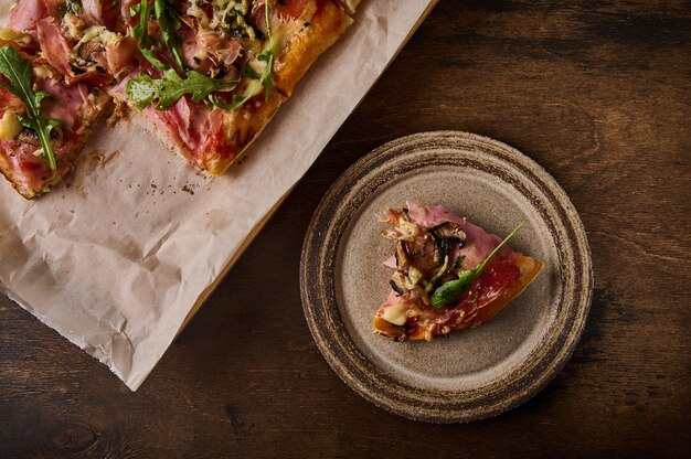 이탈리아 로마 피자 한 조각은 피자 옆에 있는 갈색 나무 배경의 소박한 세라믹 접시에 놓여 있습니다