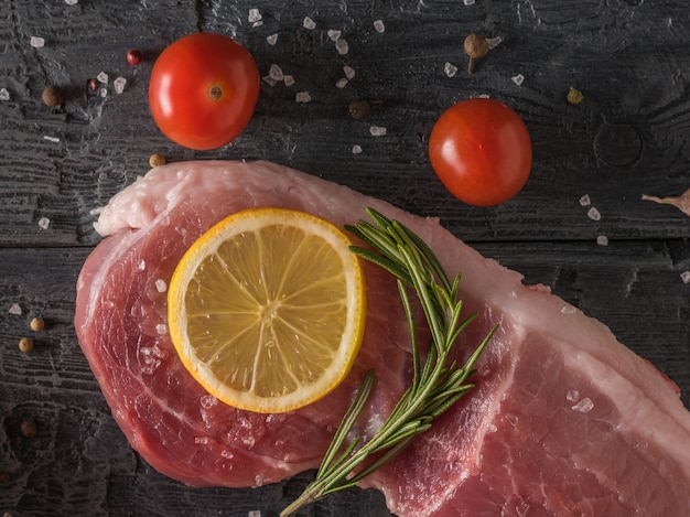 A piece of lemon and spices on a piece of pork on a black wooden table. Ingredients for cooking meat dishes.