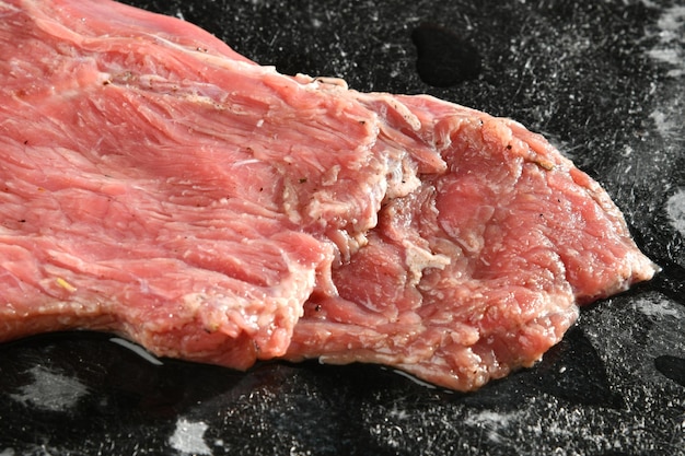 A piece of meat is being cooked on a black surface.