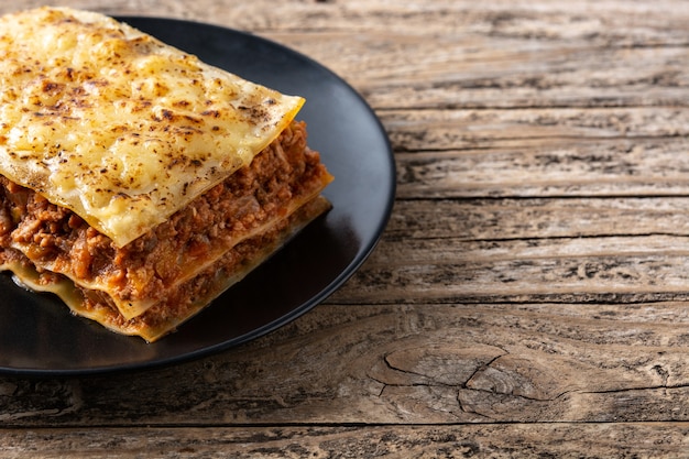 Piece of meat lasagna on black plate on rustic wooden table