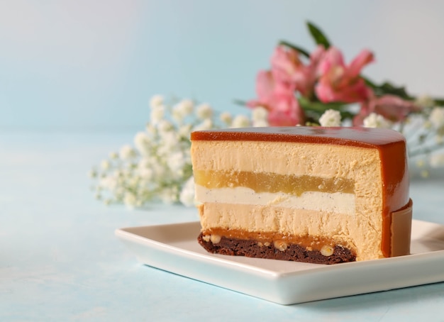 A piece of mousse cake on a square plate with flowers in the 