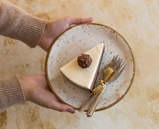 A piece of a mousse cake "three chocolate" in hand of girl, sprinkled with grated chocolate, and decorated candy