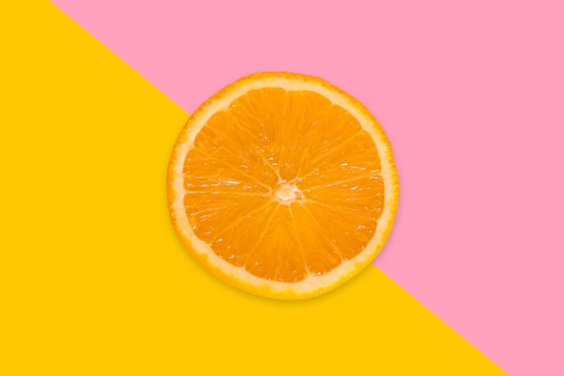 A piece of orange on a pink and yellow background View from above