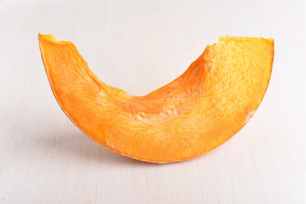 A piece of an orange pumpkin on a white wooden background