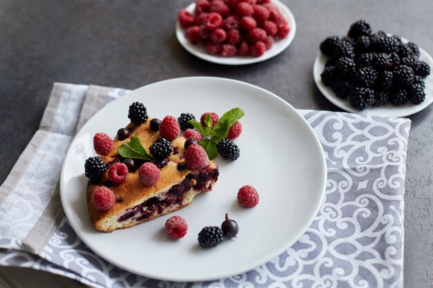 Piece of pie with blueberries, raspberry and mint for dessert on a white plate, napkin. Pieces of delicious homemade cake on a table