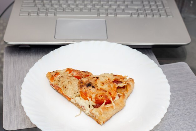 A piece of pizza lies on a plate near the computer