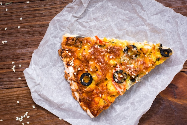 Piece of pizza with chicken, tomatoes, cheese and black olives. Top view