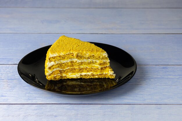 Piece of puff honey cake on black plate on blue plank surface