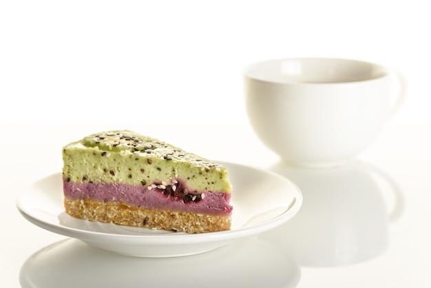 Piece of raw food cake with kiwi and blackberries on a white cup background.