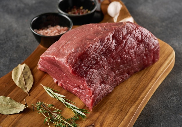 Piece of raw rump steak prepared with spices on wooden board over grey background