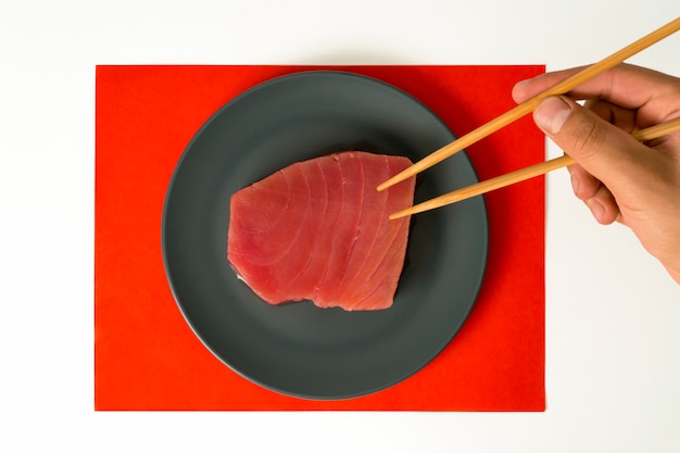 Piece of raw tuna meat and hand with chopsticks