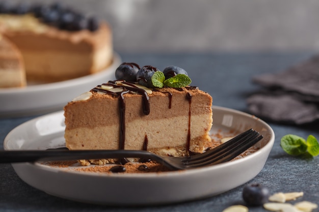 Piece of raw vegan chocolate-caramel cheesecake with blueberries and almonds. Healthy vegan food concept.