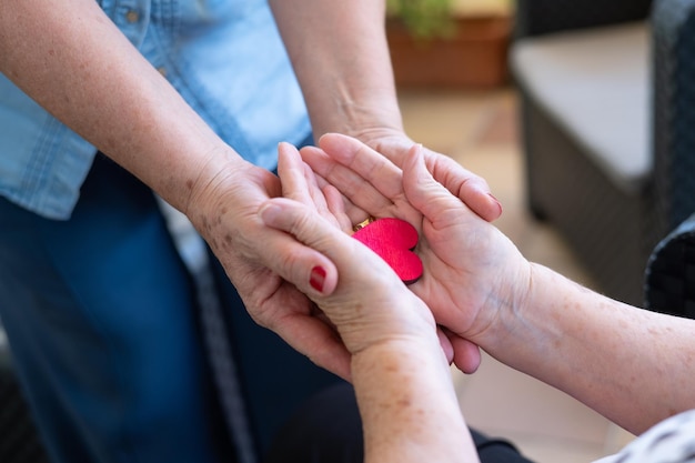 Piece Of A Red Heart In The Hands Of An Elderly Woman Next To Her Daughter