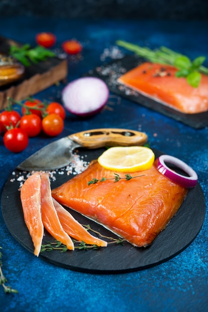 Un pezzo di pesce rosso salato si trova su una tavola di carbone con spezie.