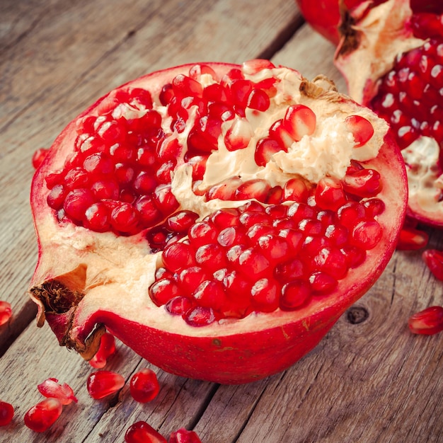 Piece of ripe pomegranate and red grains on wooden table