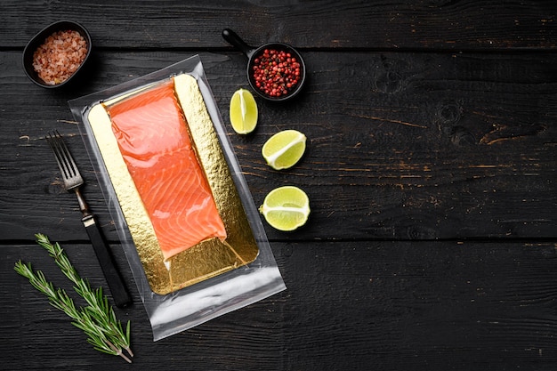 Piece of salmon fillets in a vacuum blister pack set, with herbs, on black wooden table background, top view flat lay, with copy space for text