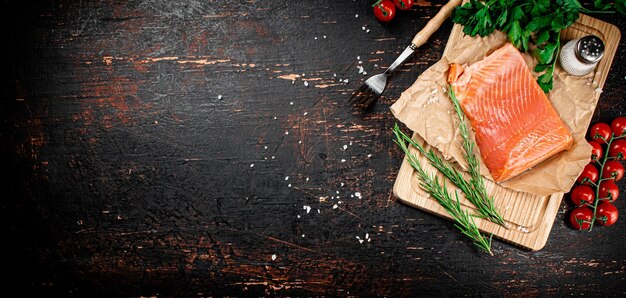 A piece of salted salmon on a cutting board with rosemary and spices