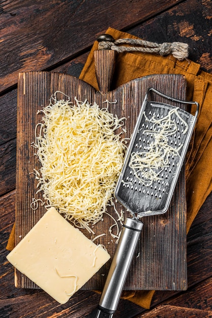 Piece of semi hard cheese and grated cheese with grater wooden\
background top view