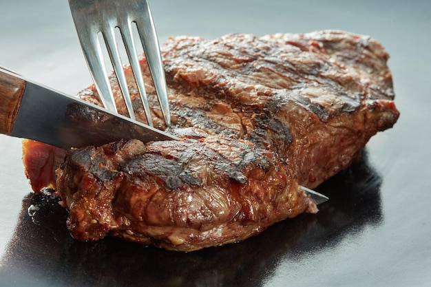 Piece of steak cut with a fork and knife on dark surface