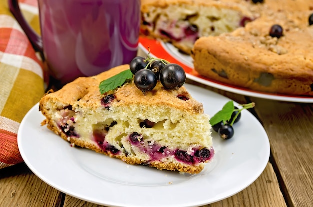 A piece of sweet cake with black currant, napkin, cup on the background of wooden boards