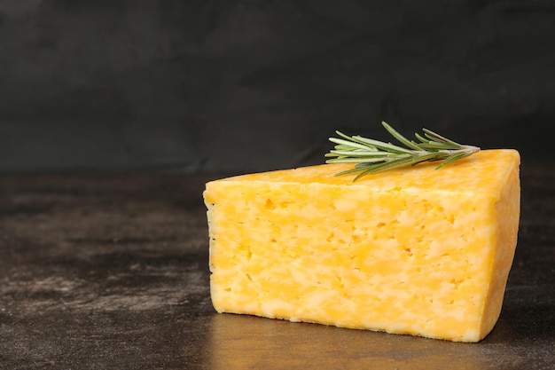 A piece of tasty marbled cheese with a sprig of rosemary on a dark background. space for text