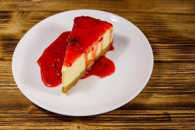 Piece of tasty New York cheesecake with raspberry jam in a white plate on wooden table