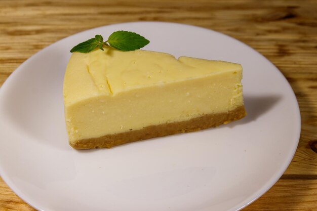 Piece of tasty sweet New York cheesecake in a white plate on wooden table