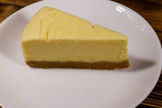 Piece of tasty sweet New York cheesecake in a white plate on wooden table