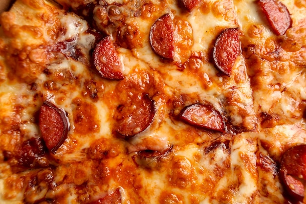 a piece of very tasty pizza with slices of hunting sausages and several types of cheese closeup