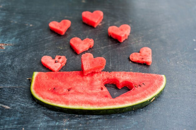 Piece of watermelon and hearts on the old wooden background. Flat lay