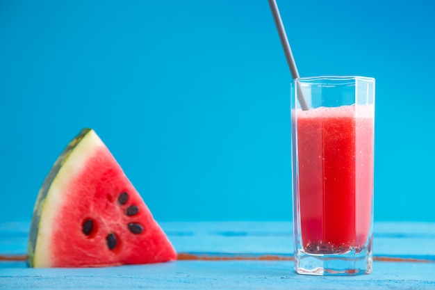 A piece of watermelon and smoothie,freshly squeezed watermelon juice in a transparent glass on a blue wooden background