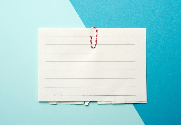 Piece of white paper in a line and a red paper clip on a blue background