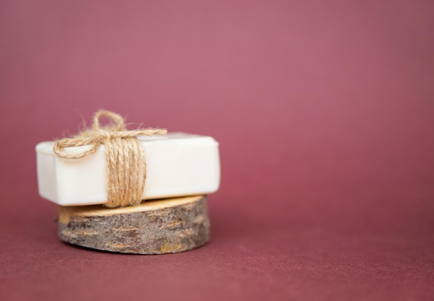 A piece of white soap lies on a cut of a tree on a burgundy background A natural organic product